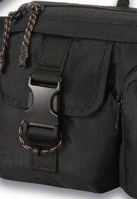 Borsa utilitaria nera in nylon con patta pieghevole, tasca laterale e una fibbia in plastica. Superficie testurizzata con cuciture e rinforzi.