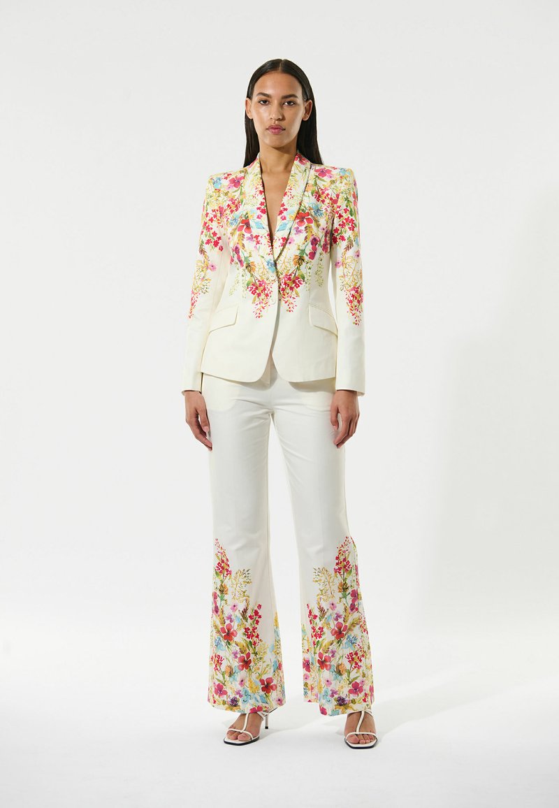 Completo floreale bianco caratterizzato da vivaci ricami in tonalità di rosa, rosso e blu. La giacca ha una vestibilità sartoriale e i pantaloni a zampa d'elefante presentano dettagli floreali.