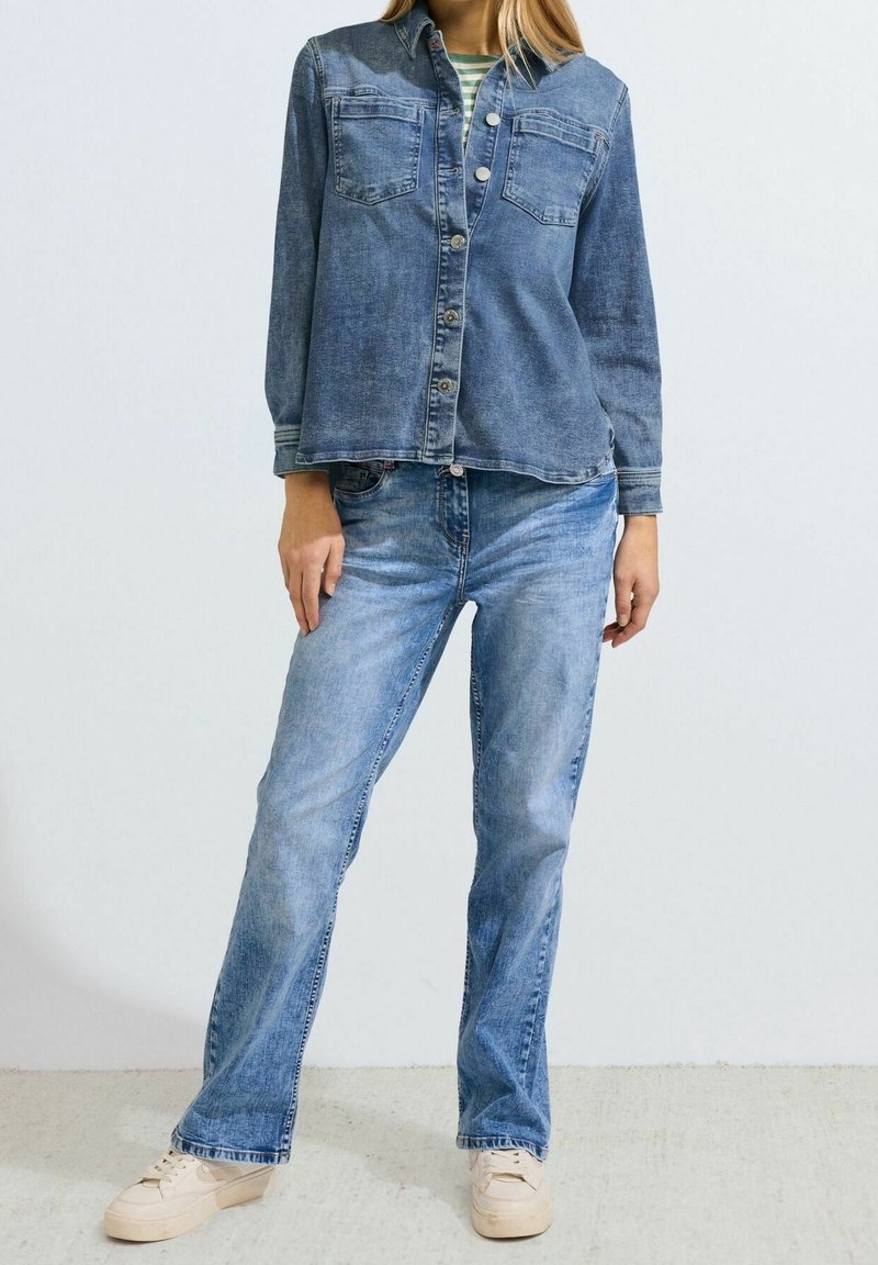 Denim-paita keskisinisessä, pitkällä hihalla, napitettuna edestä ja kahdella rintataskulla; yhdistetty vaaleansinihin suoriin farkkushortseihin ja beigen värisiin tennareihin.