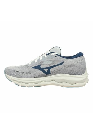Zapatilla deportiva con un upper de punto gris claro, acentos en azul marino, cordones blancos y una suela blanca acolchada con patrones ondulados para flexibilidad.