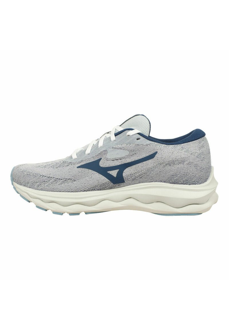 Scarpa sportiva con parte superiore in maglia grigia chiara, dettagli blu navy, lacci bianchi e una suola bianca ammortizzata con motivi ondulati per una maggiore flessibilità.