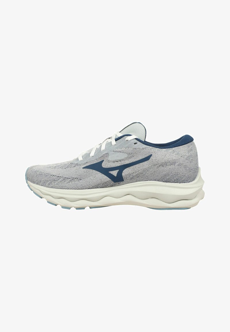 Scarpa sportiva con parte superiore in maglia grigia chiara, dettagli blu navy, lacci bianchi e una suola bianca ammortizzata con motivi ondulati per una maggiore flessibilità.