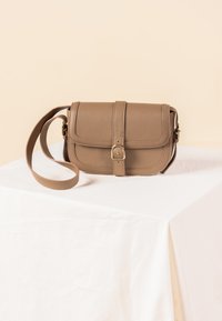 Ruskea nahkainen olkalaukku läpällä, teksturoidulla pinnalla, säädettävällä hihnalla ja kullanvärisellä solkiluksuksella. Suorakulmainen muoto.