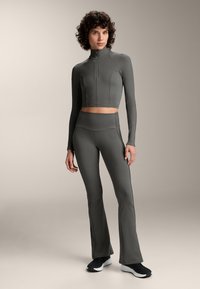 Sivá športová súprava pozostávajúca z cropped zipsového dlhého rukávu a legín s vysokým pásom a rozšírenými nohavicami, vyrobená z hladkej, elastickej tkaniny.