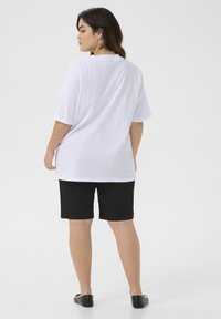 Camiseta blanca de manga corta y corte relajado, combinada con pantalones cortos negros. La tela parece suave, sin patrones ni logotipos visibles.