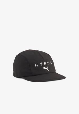 Czarna sportowa czapka z płaskim daszkiem, z białym napisem "HYROX" i logo Puma na przednim panelu, pokazana na białym tle.