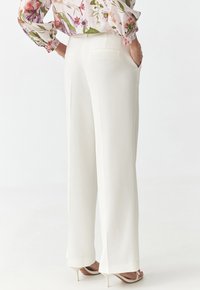 Weiße maßgeschneiderte Hosen mit geradem Bein, zwei Gesäßtaschen und einer glatten Textur, kombiniert mit hohen Sandalen.