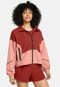 Rot und rosa farbige Blockjacke mit Reißverschluss, seitlichen Taschen und kontrastierenden Reißverschlüssen, kombiniert mit passenden roten Shorts. Glatte Stofftextur.