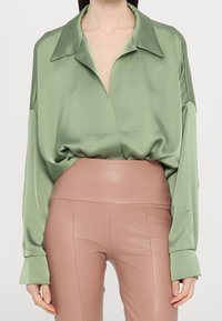 Långärmad skjorta i ljusgrön satin med krage och lös passform, kombinerad med högmidjade, åtsittande ljusrosa byxor.
