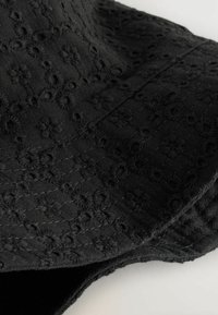 Schwarzer bestickter Stoff mit floralem Muster, versehen mit strukturierten Details und einer weichen Oberfläche, die Tiefe und visuelles Interesse schaffen.