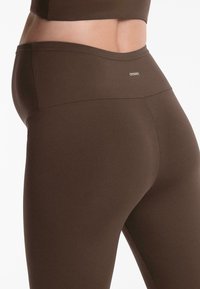Bruna högmidjade leggings gjorda av mjukt, stretchigt material. Har en logotyp på midjebandet och en slimmad, åtsittande design.