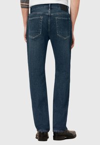 Jeans de mezclilla azul oscuro con un diseño de pierna recta, cinco bolsillos y costuras en contraste, combinados con zapatos de vestir negros.