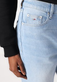Heledad sinised teksad, kitsas lõige, viie taskuga disain ja Tommy Hilfiger logo tagataskul. Pehme tekstuur ja tavaline vöökoht.