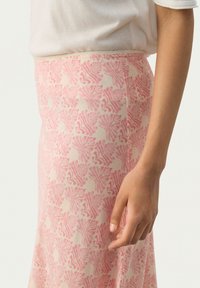 Gonna lunga in tessuto morbido con un motivo floreale rosa e crema. La silhouette è slanciata con una leggera lucentezza e una finitura liscia.