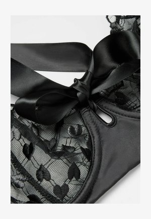 Czarny koronkowy biustonosz z sercowymi wzorami, satynową lamówką i zawiązaną satynową kokardą na gładkim tle tkaniny.