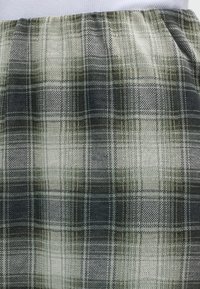 Gros plan sur un tissu de jupe à carreaux vert olive, noir et blanc avec une taille élastique, porté avec un haut clair.