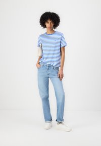 Stripet blå og hvit bomull T-skjorte med avslappet passform, paret med lyseblå denim jeans og hvite joggesko. Enkel og uformell design.