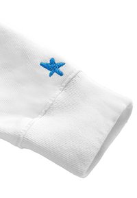 Biały bawełnowy mankiet od swetra o prążkowanej fakturze. Zdobiony małym, niebieskim haftowanym wzorem w kształcie gwiazdy w pobliżu szwu.