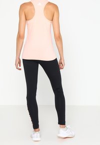 Top sin mangas de color rosa con espalda de nadadora, combinado con mallas negras que cuentan con franjas laterales, un ajuste aerodinámico y tejido ligero. Zapatillas deportivas blancas completan el conjunto.