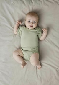 Svijetlozeleni rebrasti bodi za bebe kratkih rukava, s okruglim izrezom i kopčanjem na dnu, na svijetlosmeđem površini.