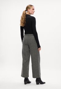 Top preto de mangas longas combinado com calças largas cinzas com padrão de pied-de-poule. Modelo usa botas de cano curto pretas com salto.