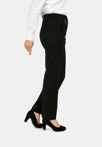Zwarte op maat gemaakte broek met een elastische tailleband, voorzien van een zijrits en een gladde textuur, gecombineerd met zwarte suède hoge hakken.
