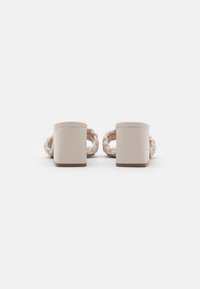 Sandales à talon bloc beige avec des brides tressées, vues de dos sur un fond blanc.