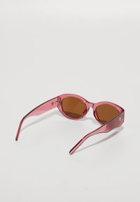 Rosa solbriller med gjennomsiktig ramme, brune linser og tynne armer. Har en rund form med minimale detaljert i maskineriet.