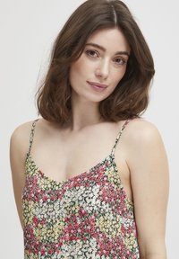 Camisola floral cu bretele subțiri, având un model de flori roșii, galbene și albe pe un fundal negru. Material ușor, cu decolteu în V.