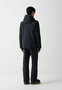 Svart isolerad jacka med huva, bakvy som visar en slät yta och design. Matchas med svarta byxor och robusta skor.