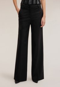 Czarne spodnie z szerokimi nogawkami, dopasowane, o gładkiej fakturze, z przednimi kieszeniami i paskiem w talii. Połączone z wzorzystym topem na ramiączkach.