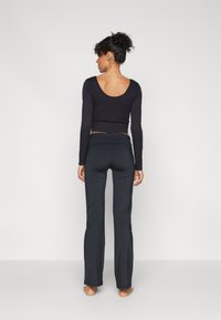 Black long-sleeve, fitted top with a scoop back paired with dark, flared yoga pants. Both garments feature a smooth, stretchy texture.
