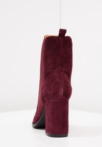 Stivale alla caviglia bordeaux con tacco alto a blocco, realizzato in suede, con una sezione in tessuto a coste e un cinturino sul retro.