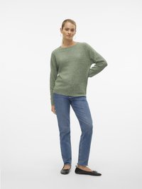 Grønn strikket genser med rund hals, lange ermer, kombinert med blå straight-leg jeans og svarte leilighetssko med sløyfer på tærne.