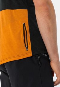 Chemise à manches courtes avec une partie supérieure noire et une partie inférieure orange. Dotée d'une poche latérale zippée et de coutures contrastantes. Tissu léger.