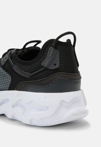 Fekete és szürke sneaker, texturált szövet felsőrésszel, párnázott bokarésszel és hullámos mintázatú fehér gumitalppal.