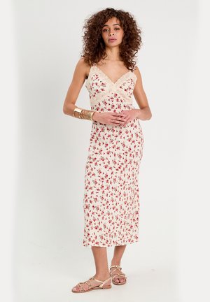 Floral midi dress with thin straps, cream background, red and green floral pattern, lace trim on neckline, smooth fabric, paired with strappy sandals.