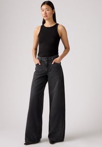 Juodas ribuotas rankovių marškinėlis, derinamas su tamsiai pilkomis, aukštos juosmens, plačiomis džinsų kelnėmis. Džinsai turi priekinės kišenes ir sagos užsegimą.