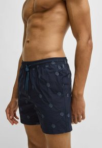 Navy swim trunks made of lightweight fabric, featuring a subtle pattern, elastic waistband with drawstring, and side pockets.