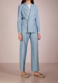 Světle modrý lněný dvouřadý blazer se zlatými knoflíky, doplněný o odpovídající kalhoty. Pod ním pruhovaná košile a béžové boty na slip-on.