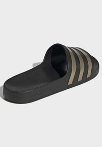 Black slide sandal with a textured rubber sole, features three wide gold stripes on the strap, and embossed logo.