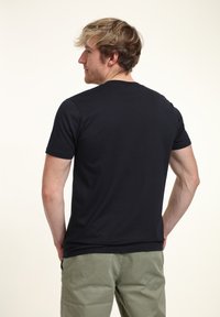 Svart kortärmad T-shirt i slät tyg, med rund halsringning. Sedd bakifrån, ihop med ljusgröna shorts.