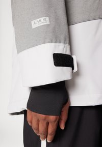 Hallist ja valge välidress, millel on Velcro mansett ja A.W.S. Extreme silt. Märkimisväärne must sisemansett ja sile tekstuuriga materjal.