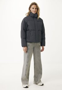 Puffjacka i mörkgrått med vita prickar, med hög krage, framdragkedja och sidofickor. Kombinerad med ljusgrå vida jeans.