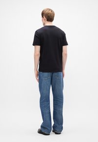 T-shirt preta de algodão com mangas curtas, combinada com jeans de ganga claros e com corte às direita, apresentando bolsos traseiros e um ajuste relaxado.