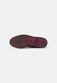 Semelle de chaussure en cuir de couleur bordeaux, avec des détails cousus et un logo en relief. Surface texturée avec un large talon pour plus de stabilité.