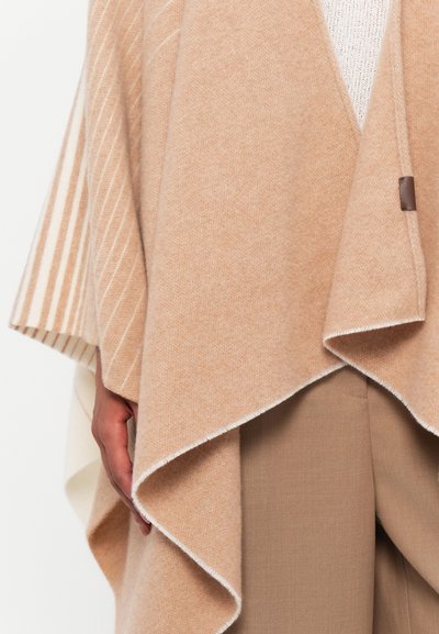 Beige ullponcho med et lagdelt design, som har myke teksturer, diagonale striper og en subtil brun hardwaredetalj.
