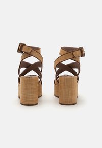 Sandalias de plataforma marrones con tiras, con un upper texturizado y tejido, que cuentan con un cierre de hebilla y un tacón chunky y cilíndrico.