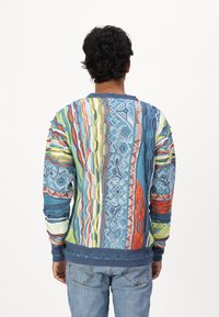 Kleurvolle gebreide trui met ingewikkelde patronen in blauw, groen, rood en geel, met ribgebreide mouwen en zoom, gemaakt van lichtgewicht stof.
