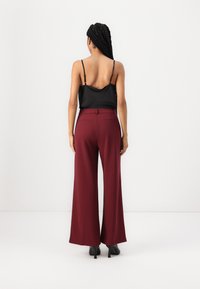 Camisole en satin noir à fines bretelles associée à un pantalon bordeaux taille haute, jambes larges. Le pantalon possède des poches arrière et une finition lisse.